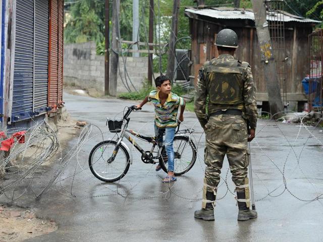 A paramilitary trooper stands guard as a Kashmiri child looks out from behind a barbed wire cordon during a curfew in Srinagar.(AFP Photo) A paramilitary trooper stands guard as a Kashmiri child looks out from behind a barbed wire cordon during a curfew in Srinagar.(AFP Photo)