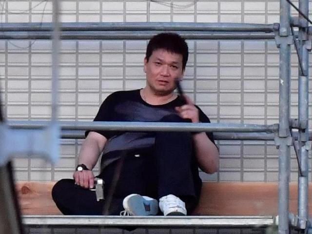Yasuhide Mizobata, a murder suspect of a fatal shooting in the city of Wakayama, holds guns as he sits on scaffoldings of an apartment building in a standoff after he fired at a police car and escaped, in Wakayama, western Japan. (REUTERS) Yasuhide Mizobata, a murder suspect of a fatal shooting in the city of Wakayama, holds guns as he sits on scaffoldings of an apartment building in a standoff after he fired at a police car and escaped, in Wakayama, western Japan. (REUTERS)