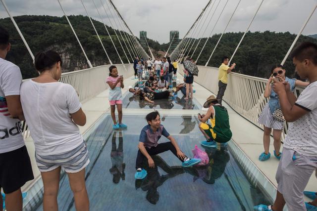 A tourist poses for a photograph on the world's highest and longest glass-bottomed bridge above a valley in Zhangjiajie in China's Hunan Province on August 20, 2016. Managers of the bridge planned to limit the number of visitors to 8,000. However, since the bridge opened, around 10,000 visitors have thronged the attraction. (AFP Photo) A tourist poses for a photograph on the world's highest and longest glass-bottomed bridge above a valley in Zhangjiajie in China's Hunan Province on August 20, 2016. Managers of the bridge planned to limit the number of visitors to 8,000. However, since the bridge opened, around 10,000 visitors have thronged the attraction. (AFP Photo)