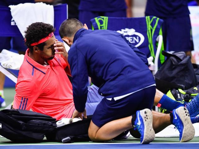 Tsonga winces as he receives assistance to his knee injury. (AFP)