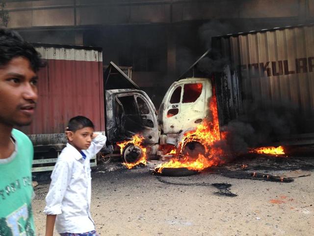People walk past as two trucks that came from Tamil Nadu and were set ablaze by protesters in Bengaluru.  (AP Photo) 