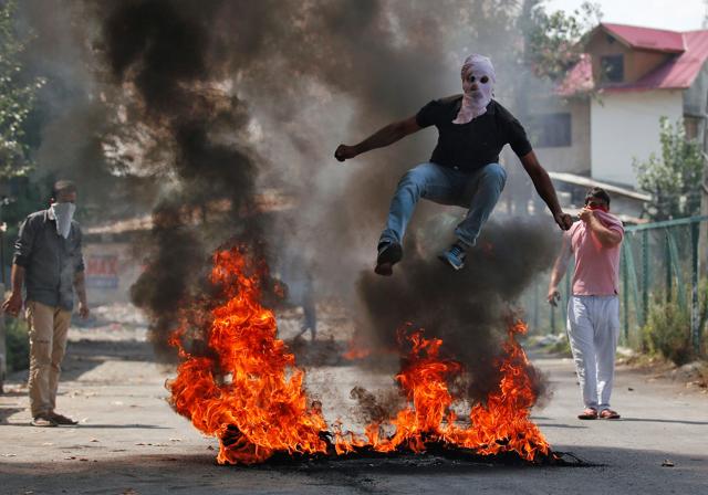 A man in a balaclava jumps over burning debris during a protest in Kashmir on Monday. (REUTERS)