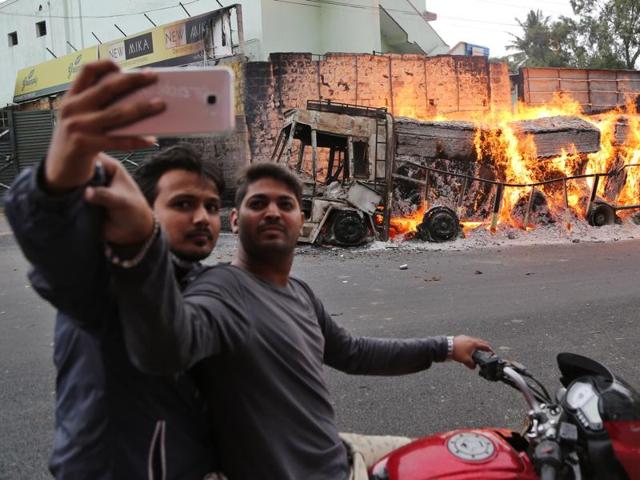Two men on a motorcycle stop to take a selfie with a burning truck in the background. (AP Photo) 