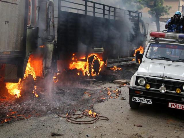 An armoured vehicle of riot police drives past burning trucks belonging to the neighbouring Tamil Nadu after they were set ablaze by angry mobs in Bengaluru. (AP Photo) 