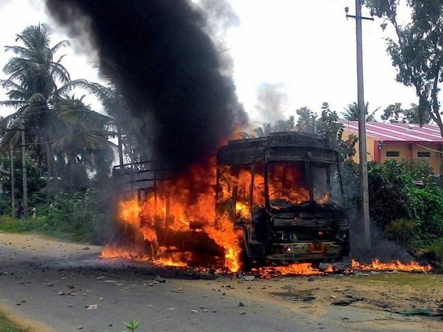 A schoolboy rides past a truck set ablaze by protesters at Hosa Guddada Halli in Karnataka on Monday.(Kashif Masood/HT Photo)