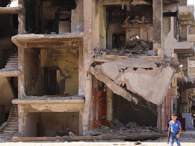A Syrian boy carries a toy gun past a destroyed building in the northeastern Syrian city of Qamishli . (AFP Photo) A Syrian boy carries a toy gun past a destroyed building in the northeastern Syrian city of Qamishli . (AFP Photo)