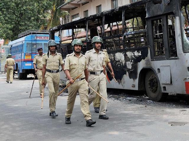 Policemen walk past a charred bus in a violence-hit Heganahalli area in Bengaluru. (PTI) Policemen walk past a charred bus in a violence-hit Heganahalli area in Bengaluru. (PTI)
