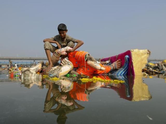 Perched on a barely submerged idol, a boy looks for scrap in the stationary waters. (Burhaan Kinu/HT PHOTO)