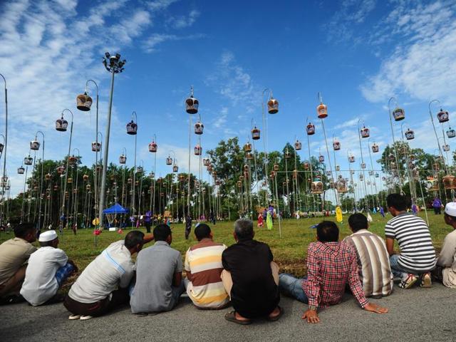 People sit and watch birds hoisted on poled in their cages during a bird-singing contest. (AFP)