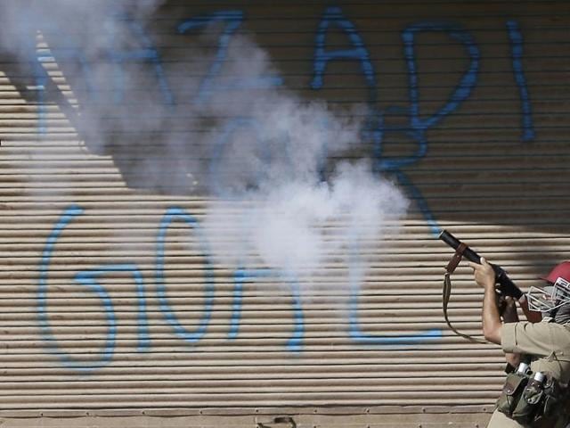 A policeman fires a tear gas shell on Kashmiri protesters in front of a graffiti on shutters that reads "Freedom our goal," in Srinagar.(AP)