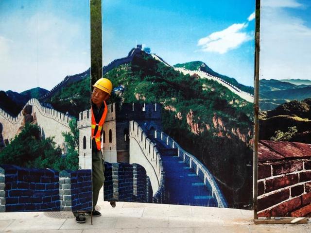 A worker looks through the fence of a construction site that is decorated with pictures of the Great Wall at Badaling, north of Beijing.(Reuters) A worker looks through the fence of a construction site that is decorated with pictures of the Great Wall at Badaling, north of Beijing.(Reuters)
