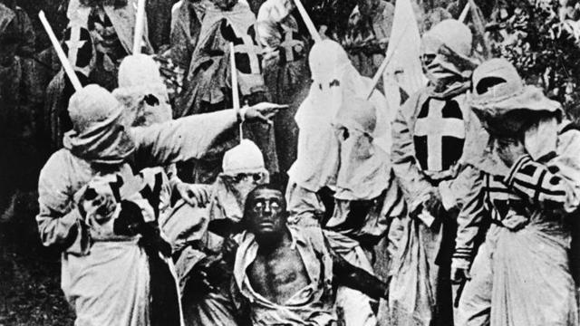 A still from DW Griffith’s The Birth of a Nation shows actors dressed as members of the Ku Klux Klan apprehending a character in blackface makeup. A still from DW Griffith’s The Birth of a Nation shows actors dressed as members of the Ku Klux Klan apprehending a character in blackface makeup.