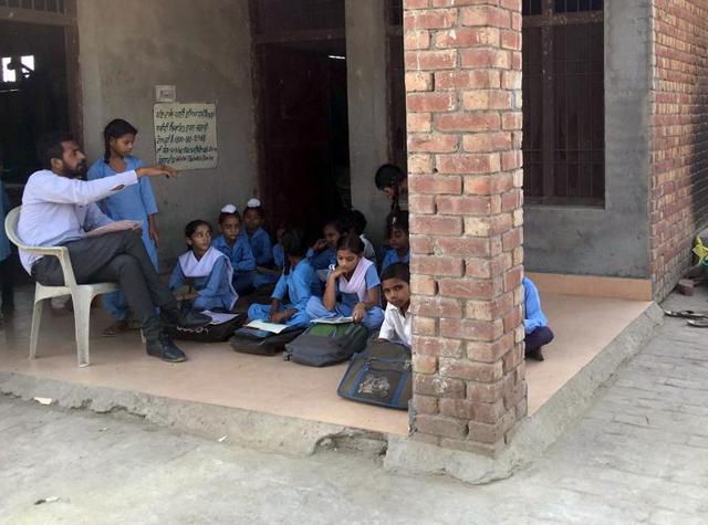Class 5 students sitting on the floor while a worker preparing mid-day meal for students in the open at the government elementary school at Kuka village near Patiala on Wednesday. (HT Photo) Class 5 students sitting on the floor while a worker preparing mid-day meal for students in the open at the government elementary school at Kuka village near Patiala on Wednesday. (HT Photo)