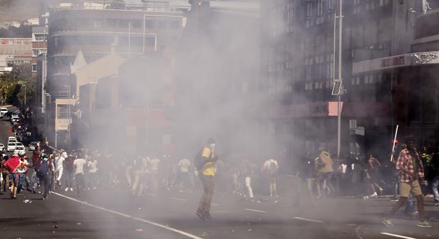 Students run after South African Police fired a stun grenade during a protest outside parliament in Cape Town, South Africa, Wednesday, Oct. 26, 2016. (AP) Students run after South African Police fired a stun grenade during a protest outside parliament in Cape Town, South Africa, Wednesday, Oct. 26, 2016. (AP)