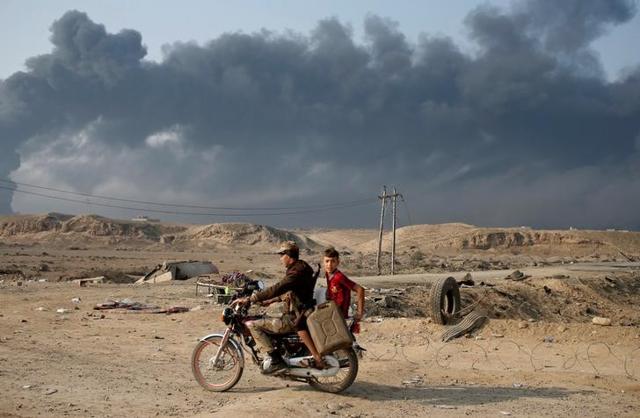 Armed members of Shi'ite militia Hashid Shaabi ride a motorbike near Qayyara, south of Mosul, Iraq. Smoke in the background is from burning oilfields set ablazed by Islamic State fighters. (Reuters) Armed members of Shi'ite militia Hashid Shaabi ride a motorbike near Qayyara, south of Mosul, Iraq. Smoke in the background is from burning oilfields set ablazed by Islamic State fighters. (Reuters)