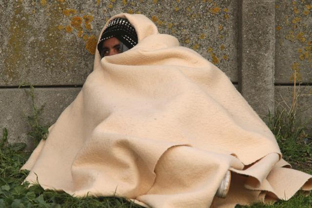 A migrant huddles under a blanket as he waits near the "Jungle" migrant camp in Calais, northern France, on October 27, 2016. A mechanical digger and other machines tore at structures in the camp, which was ravaged by fires after authorities moved in to clear the settlement. (AFP)