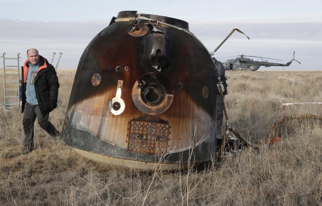 A Russian Soyuz MS space capsule stands on the ground after landing as a rescue helicopter lands nearby..  (AP Photo)