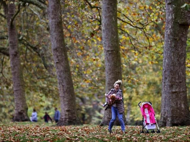 A woman swings her daughter beneath the trees in St. James's Park in London on November 1, 2016 with the trees showing Autumn colours. (AFP PHOTO / ADRIAN DENNIS)