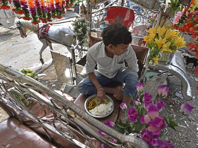 A Victoria driver takes a solitary lunch on his carriage. These drivers live on the carriages. They eat, sleep and spend all their time on the Victorias. Decked up in plastic flowers and LED lights, the carriages do run but the question mark on their future has left many such operators  clueless. (Vijayanand Gupta/HT PHOTO) 