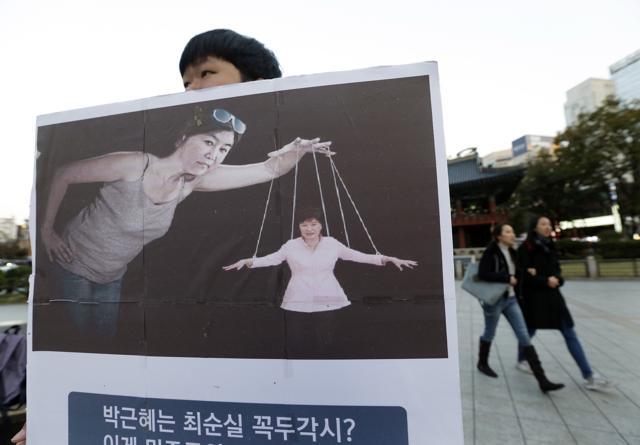 A South Korean college student holds a placard depicting South Korea's President Park Geun-hye, right bottom, as a marionette and Choi Soon-sil, who is at the center of a political scandal, as a puppeteer calling for Park to step down on the street in Seoul, South Korea. (AP) A South Korean college student holds a placard depicting South Korea's President Park Geun-hye, right bottom, as a marionette and Choi Soon-sil, who is at the center of a political scandal, as a puppeteer calling for Park to step down on the street in Seoul, South Korea. (AP)