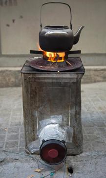 A close up shot shows a metal container outfitted with a fan that creates a highly-controlled bonfire to replace rare gas-fired stoves while using minimal firewood. (AFP Photo)