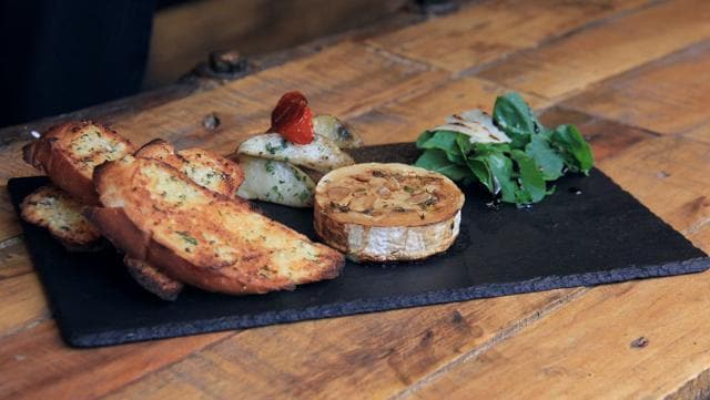 Studded with garlic cloves and topped with oregano, the oven-baked camembert was quite a treat. It is nice and runny and spreads easily on the accompanying toasted garlic bread. (Bhushan Koyande / HT Photo)