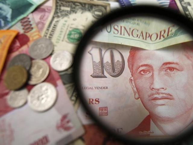 Singapore currency notes are seen through a magnifying glass among other currencies in this photo illustration. (Representative Photo) Singapore currency notes are seen through a magnifying glass among other currencies in this photo illustration. (Representative Photo)