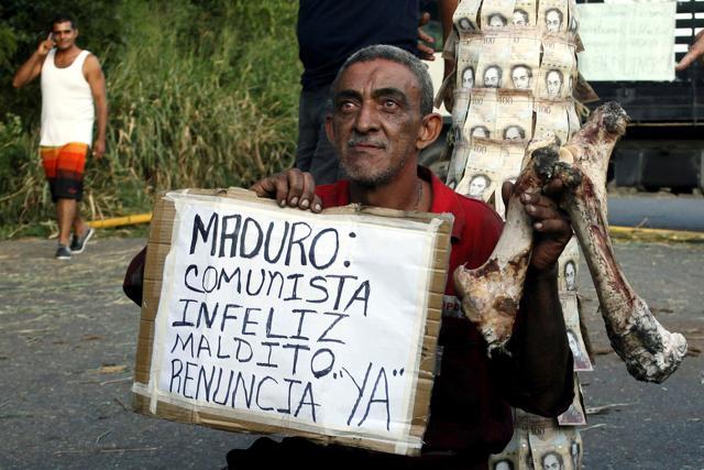 A man holds a bone and a placard that reads "Maduro: communist, unhappy, damn. Resign, now", in front of a pole covered with 100-bolivar bills during a protest in El Pinal, Venezuela. (Reuters Photo) A man holds a bone and a placard that reads "Maduro: communist, unhappy, damn. Resign, now", in front of a pole covered with 100-bolivar bills during a protest in El Pinal, Venezuela. (Reuters Photo)
