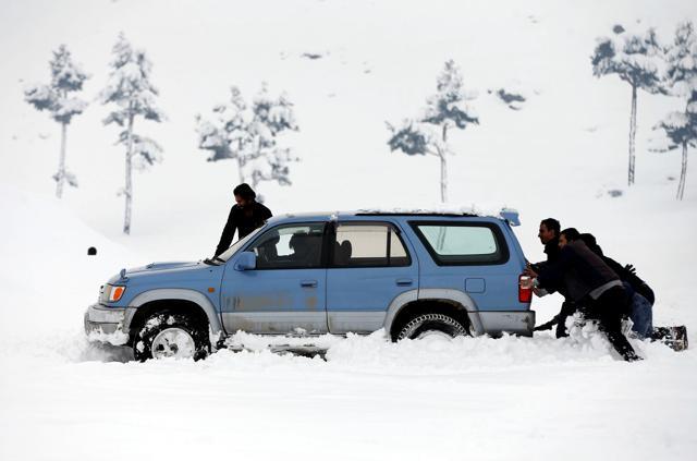 Afghan men push a car which was stuck in the snow on the outskirts of Kabul on Sunday (Reuters)