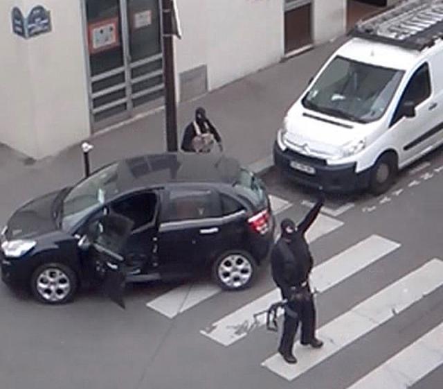 Gunmen gesture as they return to their car after an attack outside the offices of French satirical weekly newspaper Charlie Hebdo (seen at rear) in Paris on January 7, 2015. (Reuters photo)