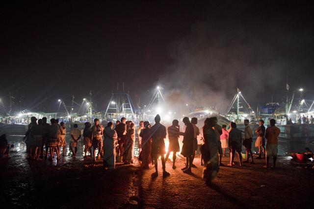 Fishermen and labourers linger around the fire at Kasimedu Fish Market to keep themselves warm after long hours in the sea in Chennai. (Saumya Khandelwal/HT PHOTO)
