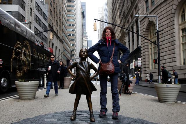 A woman poses next to a statue of a girl facing the Wall St. Bull. (Reuters Photo)