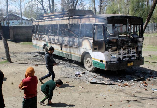 Protesters throwing stones at a burning polling staff bus after they attacked a polling station at Kanihama in Srinagar on Sunday. (PTI) Protesters throwing stones at a burning polling staff bus after they attacked a polling station at Kanihama in Srinagar on Sunday. (PTI)