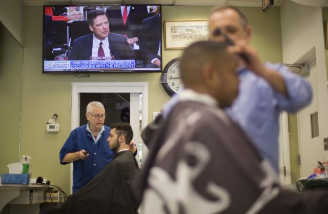 Barbers cut hair for customers as televised coverage of former FBI director James Comey testifying is seen on television screen at Puglisi Hair Cuts in the Foggy Bottom neighbourhood of Washington. (AP) Barbers cut hair for customers as televised coverage of former FBI director James Comey testifying is seen on television screen at Puglisi Hair Cuts in the Foggy Bottom neighbourhood of Washington. (AP)