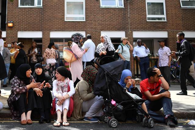People affected by the fire that ripped through Grenfell Tower, a residential block sit on the pavement outside a temporary aid centre in west London. (AFP) People affected by the fire that ripped through Grenfell Tower, a residential block sit on the pavement outside a temporary aid centre in west London. (AFP)
