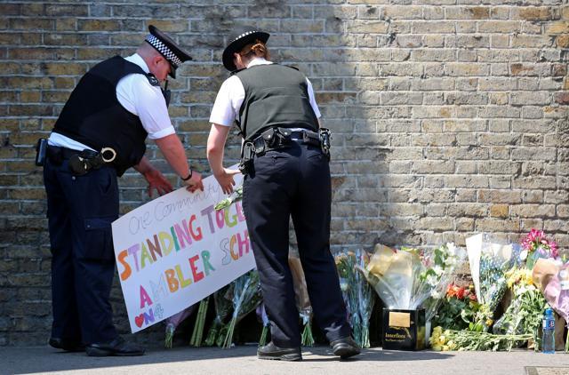 Police officers add a poster, from a local school, to floral tributes at a police cordon in Finsbury Park area of north London on June 19, 2017, following a vehicle attack on pedestrians. (AFP Photo)