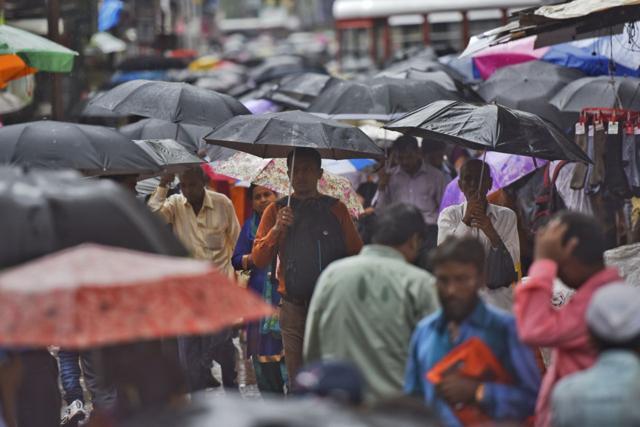 People shield themselves under umbrellas at Bhandup. Suburban trains were running late with services on the Harbour line being shut for 20 minutes at Mankhurd due to a technical problem. Trains on the Central line were running 15 to 20 minutes late. (Pratik Chorge/Hindustan Times)