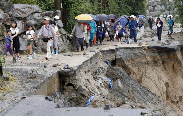 Residents walk on a damaged road to a safer place following the flooding caused by heavy rain in Asakura. (AP Photo) Residents walk on a damaged road to a safer place following the flooding caused by heavy rain in Asakura. (AP Photo)