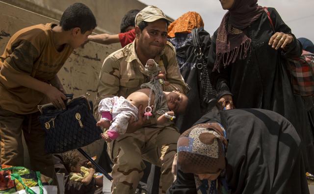A member of the Iraqi forces carries a child, as women who fled the fighting with Islamic State (IS) group jihadists in the Old City of Mosul move their belongings prior to being relocated from the city's western industrial district on July 8. (AFP) A member of the Iraqi forces carries a child, as women who fled the fighting with Islamic State (IS) group jihadists in the Old City of Mosul move their belongings prior to being relocated from the city's western industrial district on July 8. (AFP)