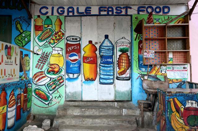 One of Sidow’s murals on the wall of a fast food store illustrating food and drinks in Wabari district of Mogadishu. (Feisal Omar / REUTERS) One of Sidow’s murals on the wall of a fast food store illustrating food and drinks in Wabari district of Mogadishu. (Feisal Omar / REUTERS)