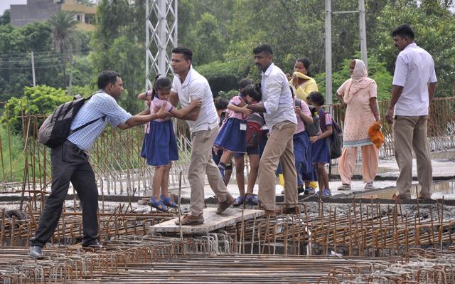 ITBP personnel helping schoolchildren cross an under-construction bridge near Manakya village at Barwala in Panchkula. (Sant Arora/HT ) ITBP personnel helping schoolchildren cross an under-construction bridge near Manakya village at Barwala in Panchkula. (Sant Arora/HT )