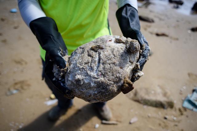 A volunteer holds a large clump of washed up palm oil. (AFP Photo) A volunteer holds a large clump of washed up palm oil. (AFP Photo)