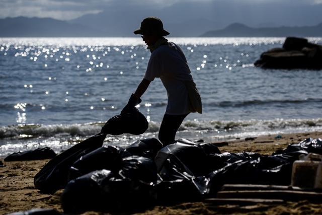 A volunteer drags a black bin bag as she helps remove washed up palm oil. (AFP Photo) A volunteer drags a black bin bag as she helps remove washed up palm oil. (AFP Photo)