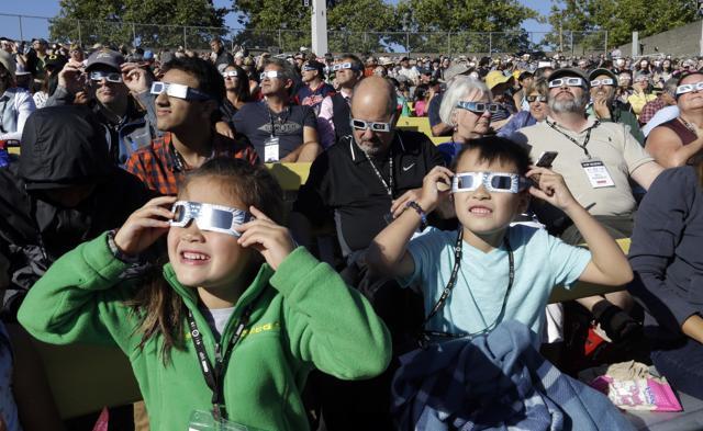 A crowd wears protective glasses as they watch the beginning of the solar eclipse from Salem, Ore., Monday, Aug. 21, 2017. (AP Photo/Don Ryan) (AP)