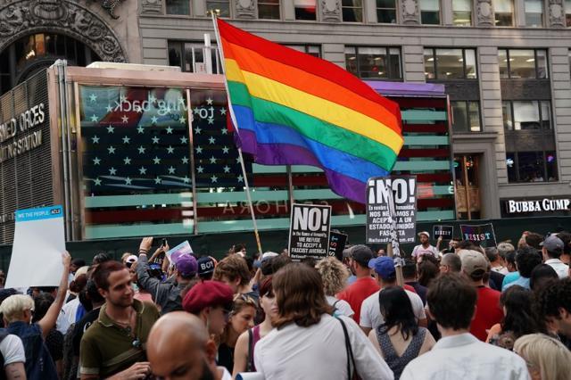 A rainbow flag flies as people protest President Donald Trump's announcement that he plans to reinstate a ban on transgender individuals from serving in any capacity in the US military, in Times Square, in New York City, New York. (Reuters) A rainbow flag flies as people protest President Donald Trump's announcement that he plans to reinstate a ban on transgender individuals from serving in any capacity in the US military, in Times Square, in New York City, New York. (Reuters)