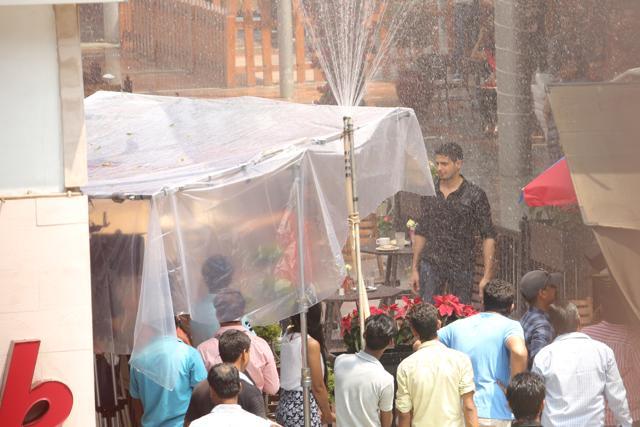 Actor Sidharth Malhotra stands next to a pipe creating ‘rain’, as onlookers watch the shoot. (Photo: Manoj Verma/HT)