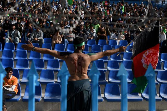 In this photograph taken on September 18, 2017 an Afghan cricket fan waves the Afghan national flag as his back has the name of Afghan national team cricket player Rashid Khan painted on it during the Shpageeza Cricket League T20 tournament at the Kabul International Cricket ground in Kabul. Thousands of cricket-mad fans have been travelling across the war-torn country to watch the domestic T20 competition. (AFP)