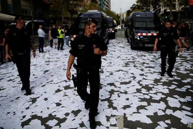 Catalan regional police officers walk through a street covered with ballots for the banned independence referendum thrown by people outside People's Party regional headquarters during a protest in Barcelona. (Reuters)