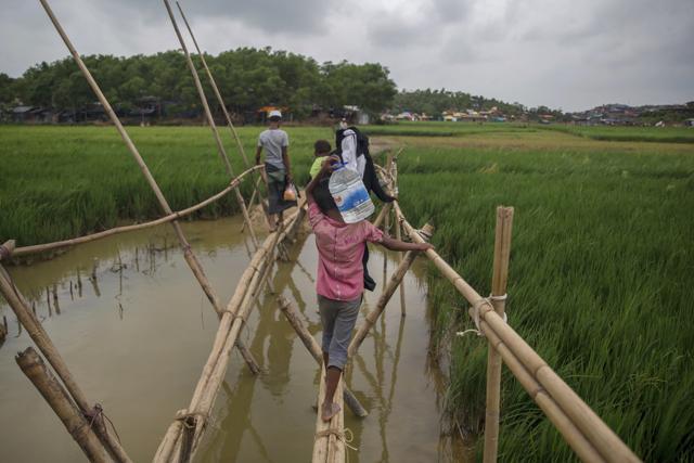 A Rohingya Muslim boy, who crossed over from Myanmar into Bangladesh, carries drinking water and crosses a flooded field on a footbridge at Thaingkhali refugee camp, Bangladesh. (AP) A Rohingya Muslim boy, who crossed over from Myanmar into Bangladesh, carries drinking water and crosses a flooded field on a footbridge at Thaingkhali refugee camp, Bangladesh. (AP)
