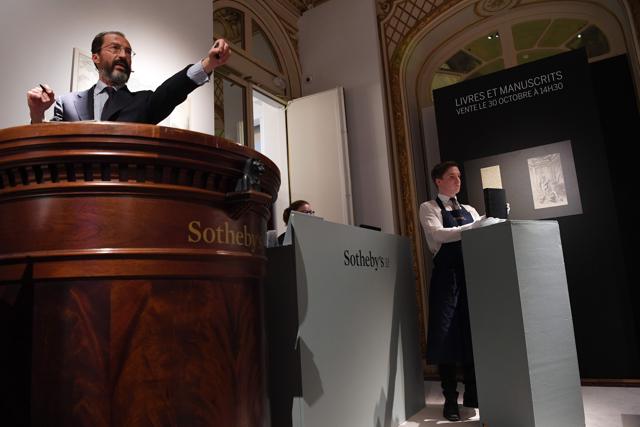 An assistant holds a copy of the manuscript as the auctioneer (L) gestures during the auction sale. (Christophe Archambault/AFP) An assistant holds a copy of the manuscript as the auctioneer (L) gestures during the auction sale. (Christophe Archambault/AFP)
